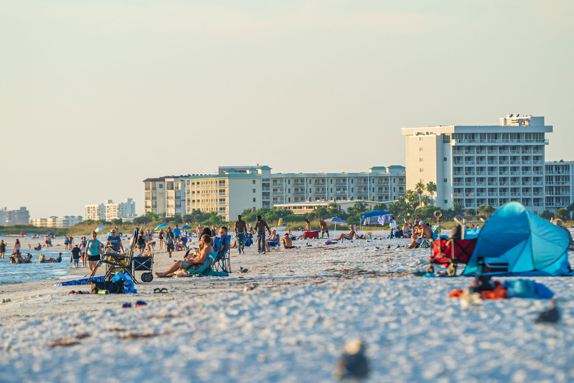 A beach scene with people and buildings in the background.